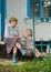 A little girl and an old woman are sitting on the steps of their old house. A little girl eats straws of biscuits and shares them