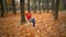 Little girl in orange helmet and protective gear on rope-way in autumn  forest. smiling child engaged climbing rope park.