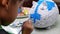 A little girl paints with a brush on the figure of a white pig-shaped papier-mache at home. Make your own piggy bank.