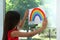 Little girl with picture of rainbow near window.  Stay at home concept