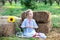 Little girl with pigtail on her head sits on roll of haystacks in garden and holds sunflower. Child sits on straw and enjoys natur