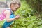 A little girl with pigtails in a bright dress sitting near a bush of wild strawberry. side view