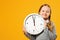 Little girl with pigtails holds a big clock on a yellow background. The concept of education, school, timing, time to learn.