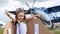 A little girl in a pilot`s costume with cardboard wings runs on the lawn against the backdrop of the plane. A child in a