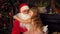 A little girl in a pink dress sits on Santa`s lap and hugs him