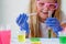 A little girl in pink glasses conducts experiments. A child in rubber gloves takes a red liquid with a pipette and adds it to the