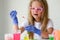 A little girl in pink glasses conducts experiments. A child in rubber gloves takes a red liquid with a pipette and adds it to the