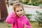A little girl in a pink hoodie with a sad and tearful face is holding her ear. Ear pain, otitis media, swelling of the cheek, gums
