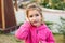 A little girl in a pink hoodie with a sad and tearful face is holding her ear. Ear pain, otitis media, swelling of the cheek, gums