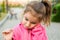 A little girl in a pink hoodie with a sad and tearful face is holding her ear. Ear pain, otitis media, swelling of the cheek, gums