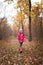 Little girl in pink jacket, knit cap and resin boots happily running in autumn forest on golden leaves cover