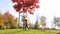 A little girl in a pink jacket runs in a park near a tree with red leaves