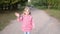 a little girl in a pink jacket walks along a walking path in the park