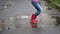 A little girl in pink rubber boots jumps in a puddle on a summer day. Close-up, slow motion