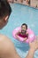 Little girl with a pink tube and her father swimming in the pool