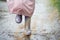 Little girl in pink waterproof raincoat, purple rubber boots funny jumps through puddles on street road in rainy day