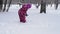 A little girl in a pink winter jumpsuit plays with snow.
