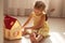 Little girl playing with doll house while siiting on floor in bedroom. Role game for young children. Female child putting to bed