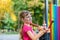 A little girl is playing on a multi-colored xelophon in the park. The child is beaten with hammers on a street musical instrument