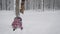 Little girl playing with snow, clearing himself a path in snow-covered park in winter. Child actively pursuing their