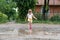 Little girl is playing in the water in the middle of a ruined road, after rain