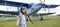 A little girl plays a pilot on the background of a small plane with a propeller. A child in a suit with cardboard wings