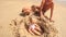 Little Girl Plays in Sand Hole by Grandpa Boy on Beach