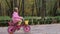 Little girl practice to ride a pink bicycle in the autumn park