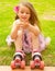 Little girl preschool beginner in roller skates, putting some grass in her hand, grass background