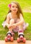 Little girl preschool beginner in roller skates, putting some grass in her hand, grass background