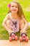 Little girl preschool beginner sitting in the grass with her roller skates, in a grass background