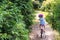 Little girl in a protective helmet rides a two wheeled pink bike in a beautiful park on a sunny