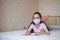 Little girl in a protective mask writes in a notebook during quarantine. Distance learning education. look at camera