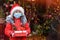A little girl in a protective medical mask holds a gift box against the background of a Christmas background. Safe Xmas and new