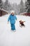 Little girl is pulling her snow scooter with a toy