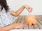 Little girl putting coin into piggy bank for saving with pile of