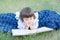 Little girl reading book lying on stomach outdoor, smiling cute child, children education and development. Kids outside activity.