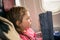 A little girl reads the menu on the plane. A child is sitting near the window of an aircraft. Baby travels by plane and reads a