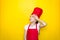 Little girl in a red chef`s suit girl is tired of cooking, wipes his hand forehead on yellow background with copy space