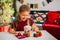 Little girl in red dress eating Christmas cookies with cacao in cup, red Chirstmas decorations around