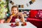 Little girl in red dress eating Christmas cookies with cacao in cup, red Chirstmas decorations around