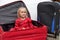 Little girl in a red elegant dress sits in a suitcase