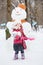 Little girl with red plastic shovel stands against snowman