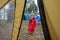 A little girl in a red raincoat with a hood eats candy on a stick in the forest, a view from a tourist tent. Children`s outdoor re