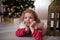 Little girl in red sweater lie under the Christmas tree and wait for a miracle