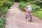 Little girl rides a two wheeled pink bike in a beautiful park on a summer day