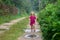 Little girl in rubber boots runs through muddy puddles along a country sandy road after rain