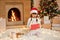Little girl`s excitement from opening presents on Christmas, female child sitting on floor in santa hat, keeps mouth opened, bein