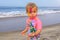 A little girl on a sandy beach against the background of sea waves with a painted face, Indian holiday Holy, sun glare and color