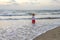 A little girl on a sandy beach against the background of the setting sun went into the sea and looks into the distance,